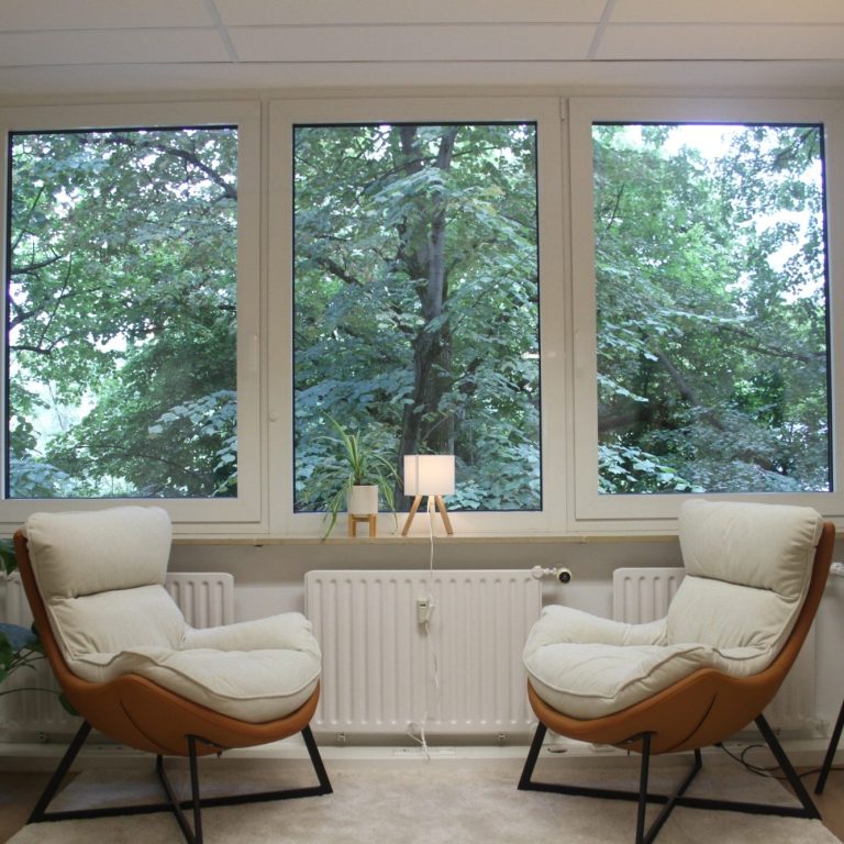 Mein Praxisraum Zwei bequeme Sessel vor einem Fenster mit Blick auf Bäume und Natur.